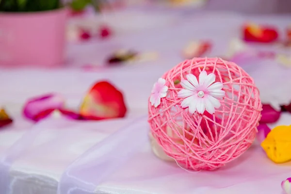 Thread pink bauble with artificial flowers and flower petals on the table