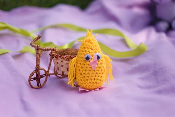 Handmade knitted chicken toy with wicker bicycle standing on pink plaid. Easter and spring decorative elements concept.