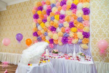 Beyaz dantel beşik, balonlar, çikolatalar, beyaz mumlar ve masanın üzerinde çiçek yaprakları. Kağıt çok renkli çiçek duvarı arkaplanı.