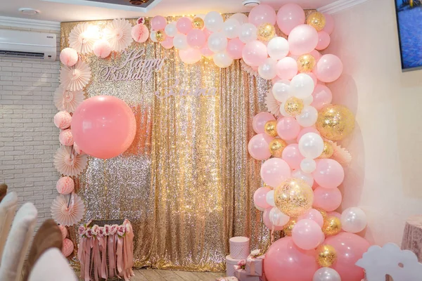 Beautiful pink decorations, wrapped present boxes with ribbons and bow, flowers and balloons on golden shiny background. Little girl birthday party decorations.