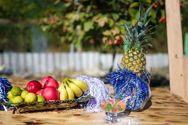 Pineapple, apples, banana and lime on wooden table. Festive table for outdoor summer party.