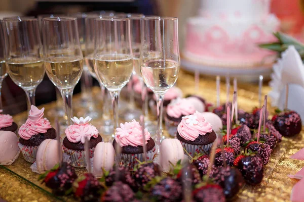 软硬集中拍摄的节日糖果酒吧与杯蛋糕 香槟酒杯和草莓巧克力釉面 背景上没有聚焦的粉色蛋糕 婚礼或生日派对的概念 — 图库照片