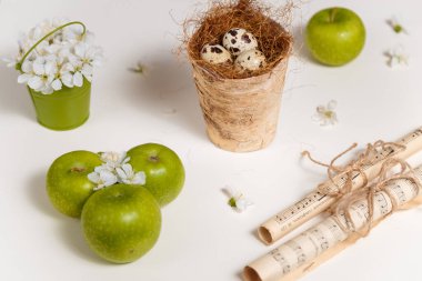 Paskalya ve bahar konsepti. Bıldırcın yumurtaları, yeşil kovada kiraz çiçekleri, yeşil elmalar ve beyaz arka plan üzerine not kağıdı..