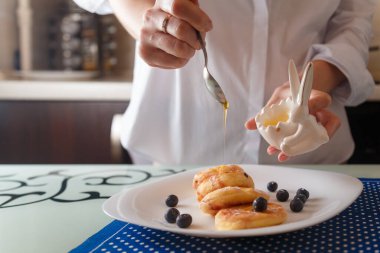 Geleneksel şurup ya da süzme peynirli pankaces ile yaban mersini ve beyaz tabakta mavi peçeteli bal karıştıran kadın elleri. Sağlıklı kahvaltı, diyet konsepti.