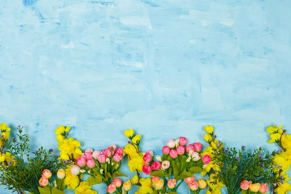 Artificial pink and yellow flowers on blue painted wooden background. Spring blossom, Easter, women day, mothers day, 8 March concept. Copy space.