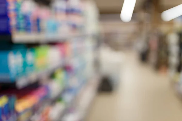 Unfocused shot of supermarket interior. Blurry hypermarket, mall or shopping center background. Rows and shelves with household chemicals for washing and cleaning.