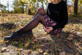 Nő fekete pulóverben és pólóban, virágokkal az őszi erdőben. Női kéz piros manikűrrel ölelő lábak szürke cipőben.