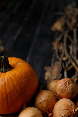 Siyah ahşap arka planda kuru sonbahar dalları olan balkabağı ve soğan. Sonbahar hasadı, sağlıklı organik gıda konsepti. Boşluğu kopyala.