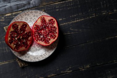 Siyah ahşap zemin üzerinde iki parça nar meyvesi. Boşluğu kopyala