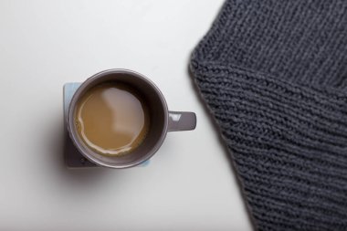 Beyaz masa arkasında bir fincan sıcak kahve ya da kakao ve gri örgü eşarp. Sıcak sonbahar ya da kış, sıcak içecekler, ev yapımı içecek konsepti..