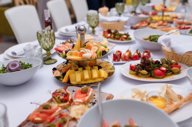 Dilimlenmiş meyveli şenlik yemeği. Mango, muz, kivi ve narenciye. Kanepe ve sebze salatası. Beyaz masa örtüsü ve peçeteler. Restoranda ya da kafede düğün ya da doğum günü masası.
