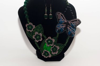 Kelebek şeklinde boncuklu kolye ve beyaz arka planda siyah göğüslü çiçekler. Kadın aksesuarları, dekoratif süsler ve mücevherler. Moda ve tarz kavramı.