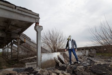 Gaz maskeli insan harabeler ve dramatik gökyüzü arkaplanı arasında duruyor. Çevresel kirlilik, ekoloji felaketi, radyasyon, biyolojik tehlike kavramı.
