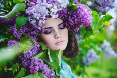 Güzel bir kızın portresi, yumuşak makyajlı ve başında büyük leylak çiçekli bir çelenk. Güzel vesikalık, bahar çiçeği konsepti..