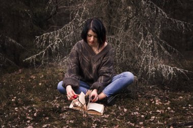Genç bir kadın doğada bir kitabı ateşe veriyor.