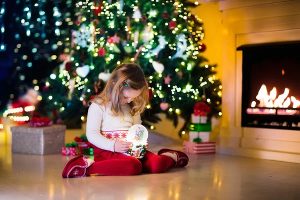 Niña sosteniendo bola de nieve bajo el árbol de Navidad — Foto de Stock