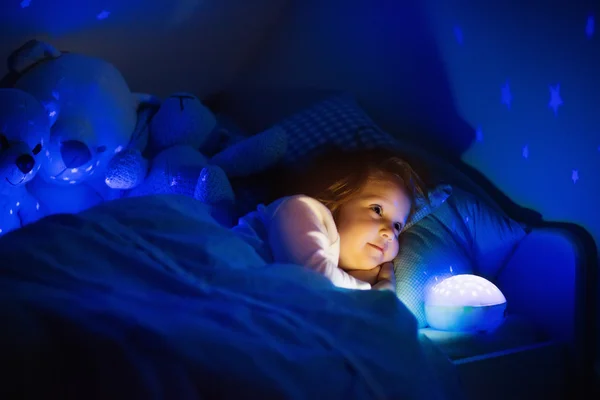 Lilla flickan i sängen med natt lampa — Stockfoto