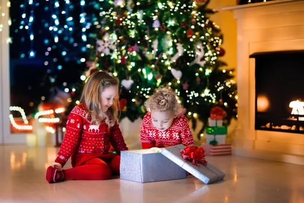 Kinderen openen Kerstcadeaus bij open haard — Stockfoto