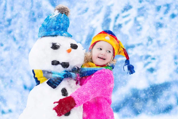 Malá holčička budování muž sněhu v zimě — Stock fotografie