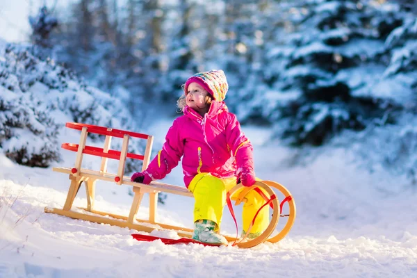 Маленькая девочка веселится на санях в снежном зимнем лесу — стоковое фото