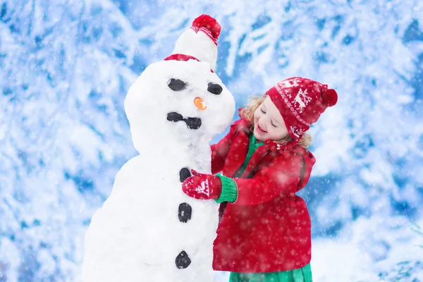 Menina construindo um homem de neve no inverno — Fotografia de Stock