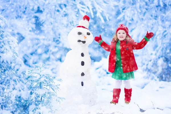 Liten flicka bygga en snögubbe på vintern — Stockfoto