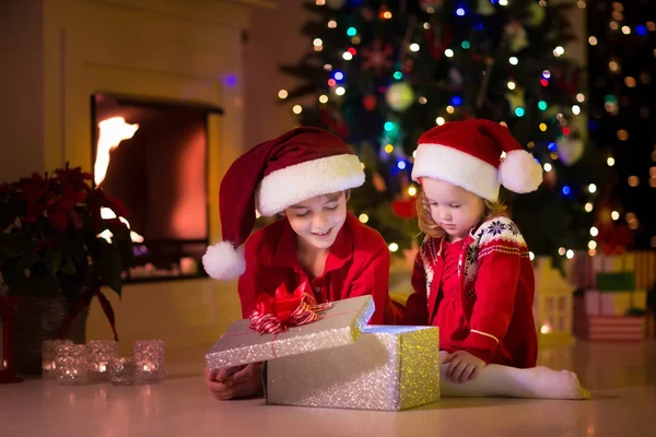 Kinderen openen Kerstcadeaus bij open haard — Stockfoto