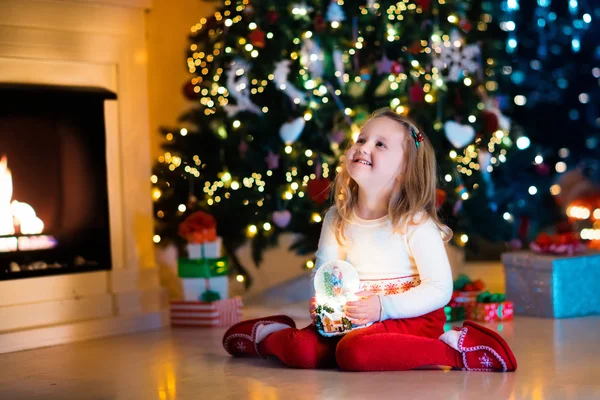 Liten flicka håller snowjordklot under julgranen — Stockfoto