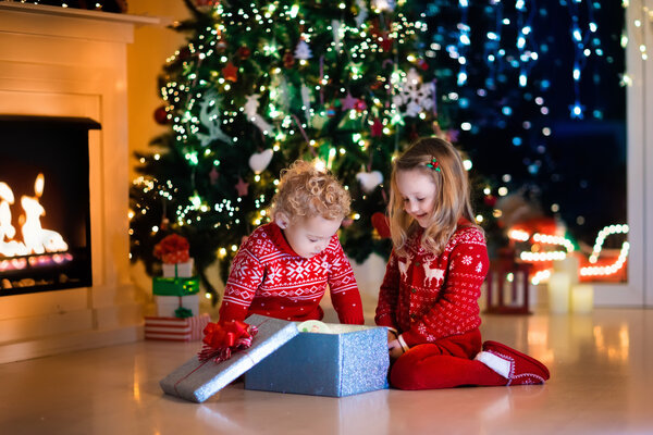 Kids opening Christmas presents at fireplace