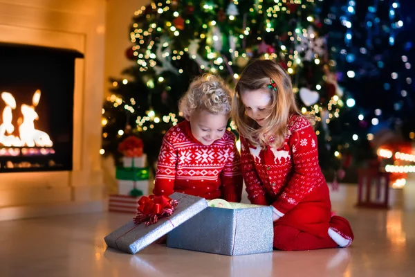 Kinderen openen Kerstcadeaus bij open haard — Stockfoto