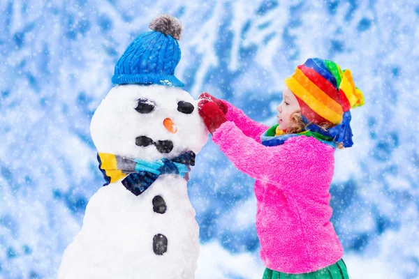 Malá holčička budování muž sněhu v zimě — Stock fotografie