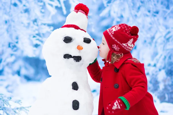 Liten flicka bygga snögubbe på vintern — Stockfoto