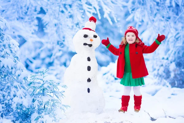Küçük kız bir kar adam kışın bina — Stok fotoğraf