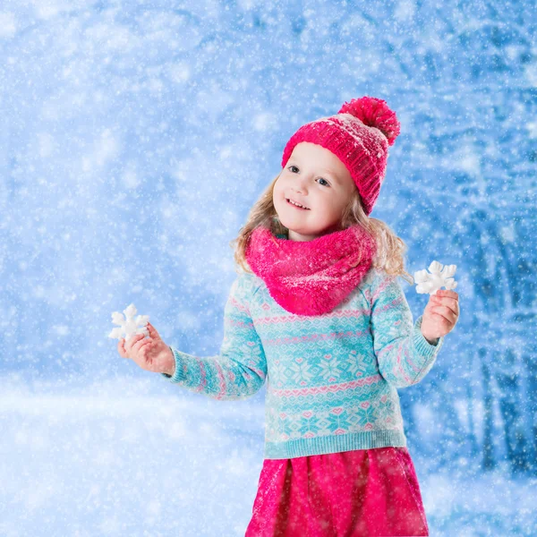 Little girl playing with toy snow flakes in winter park — Stock Photo, Image