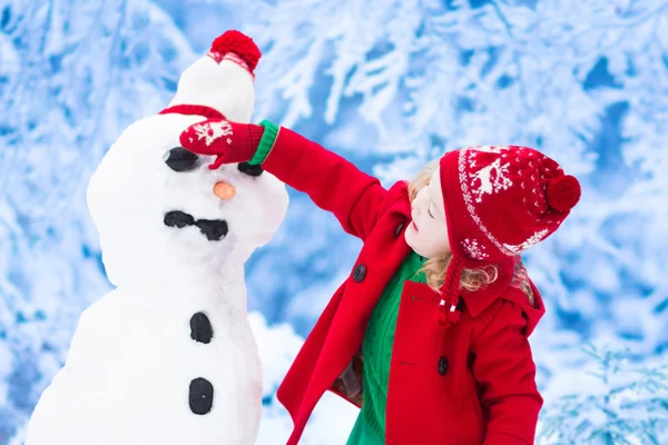 Menina construindo um homem de neve no inverno — Fotografia de Stock