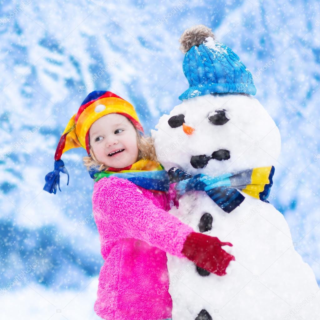 Little girl building a snow man in winter