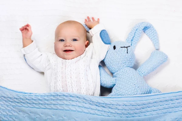 Baby boy playing with blue knitted bunny toy — Stock Photo, Image