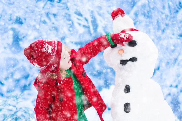 Menina construindo um homem de neve no inverno — Fotografia de Stock