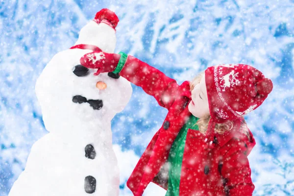 Küçük kız bir kar adam kışın bina — Stok fotoğraf