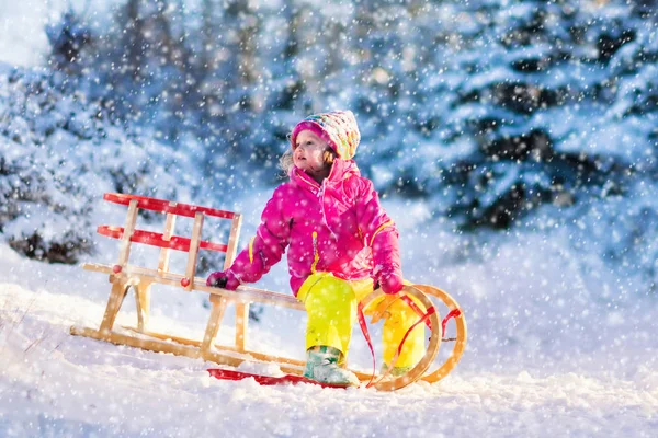 Маленькая девочка веселится на санях в снежном зимнем лесу — стоковое фото