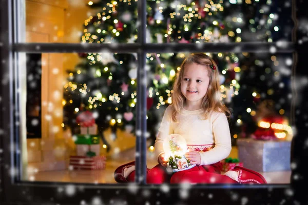 Niña sosteniendo bola de nieve bajo el árbol de Navidad — Foto de Stock