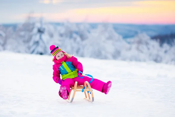 Bambino che gioca sulla neve sulla slitta nel parco invernale — Foto Stock