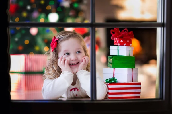 Kleines Mädchen öffnet Weihnachtsgeschenke am Fenster — Stockfoto