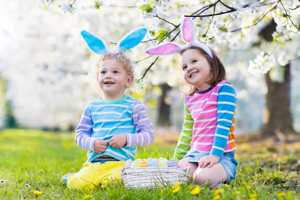 Caza de huevos de Pascua. Niños con orejas de conejo en jardín de primavera . —  Fotos de Stock