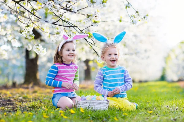 Caza de huevos de Pascua. Niños con orejas de conejo en jardín de primavera . — Foto de Stock