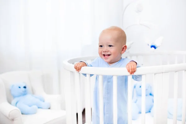 Baby pojke stående i säng i vit plantskola — Stockfoto