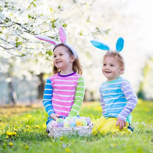 Caccia alle uova di Pasqua. Bambini con orecchie da coniglio in giardino primaverile . — Foto Stock