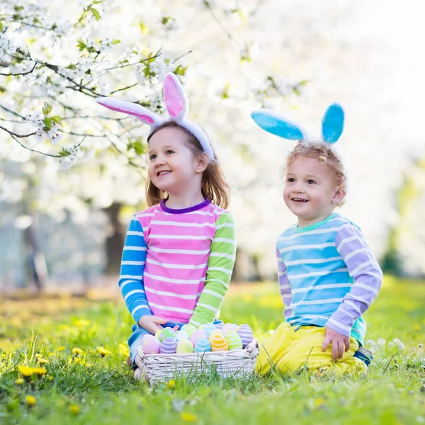 Caza de huevos de Pascua. Niños con orejas de conejo en jardín de primavera . — Foto de Stock