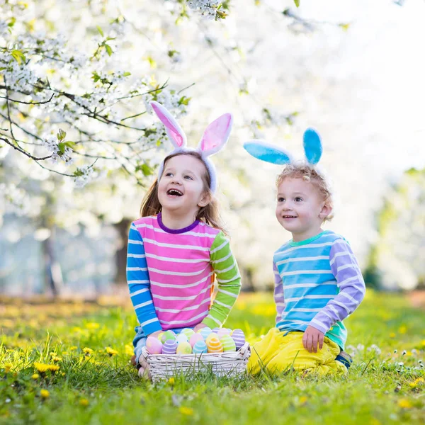 Caza de huevos de Pascua. Niños con orejas de conejo en jardín de primavera . — Foto de Stock
