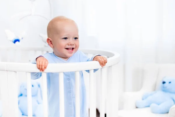 Baby boy standing in bed in white nursery — Stock Photo, Image